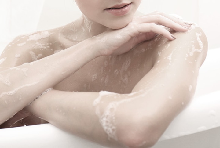 Mujer en la tina con espuma de jabón cubriendo su piel y hombros durante un baño relajante.