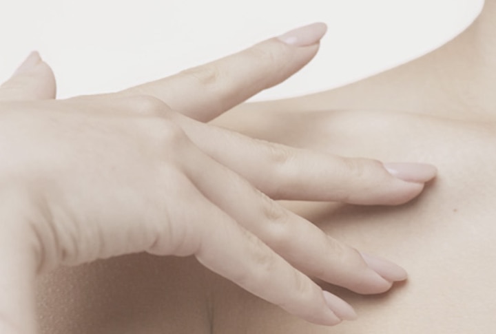 Mano de mujer con manicura natural tocando suavemente su hombro y piel tersa sobre un fondo blanco.